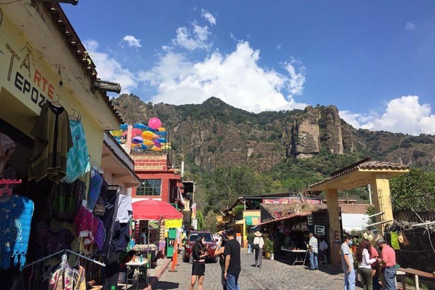 Un vivace mercato di strada con bancarelle colorate, una montagna imponente sullo sfondo e una grande formazione rocciosa. 4
