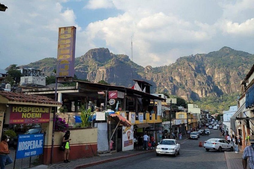 Una strada fiancheggiata da edifici, con una montagna sullo sfondo e un cartello di un albergo. 2