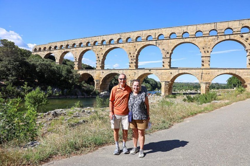 A stone aqueduct with multiple arches, a paved path, and greenery. 2