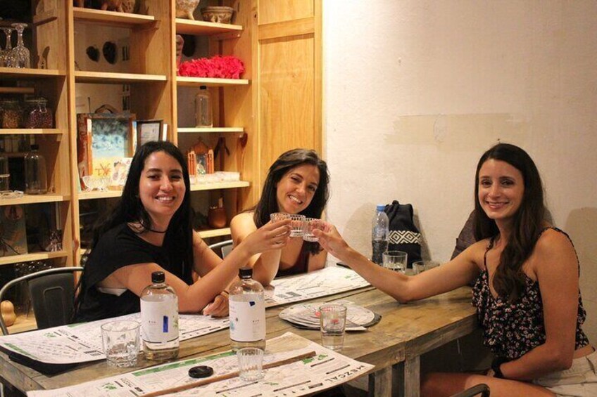 Three women toasting with glasses at a wooden table with papers and bottles. 4