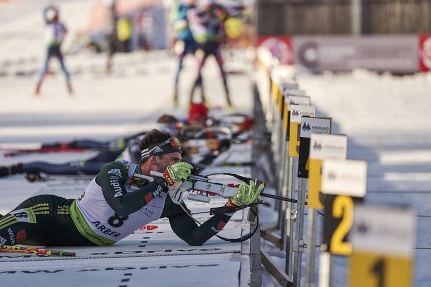 Un esquiador de fondo en movimiento, con uniforme verde y blanco, compite en una pista nevada con balizas numeradas. 2