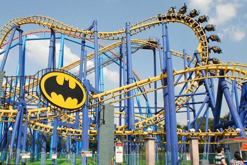Eine Achterbahn mit Batman-Logo, blau-gelben Gleisen und wolkenlosem Himmel. 4