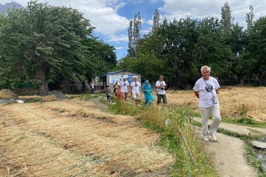 A group of people walking on a dirt path in a rural area with trees and a small building in the background. 5