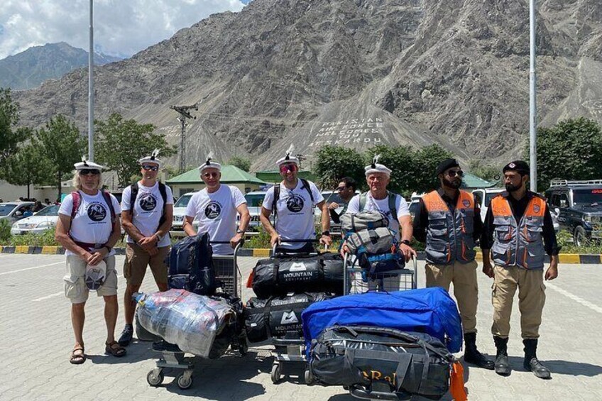 A group of people with luggage in a parking lot with mountains in the background. 1