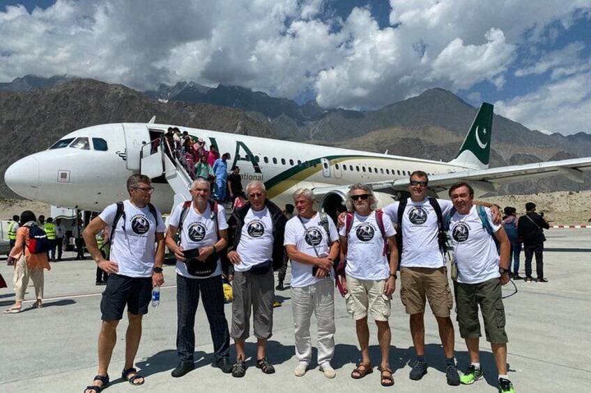 A group of people standing in front of an airplane with a mountainous landscape in the background. 1