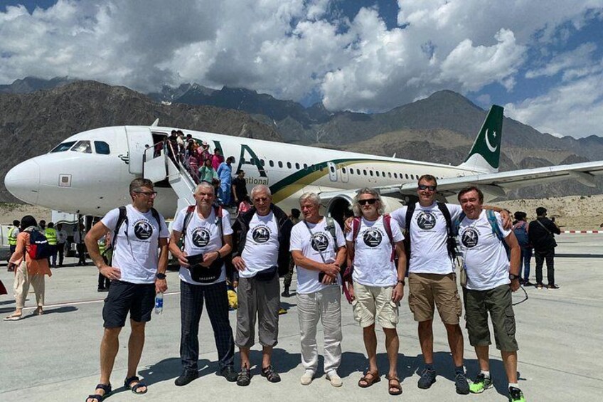 A group of people standing in front of an airplane with a mountainous landscape in the background. 1
