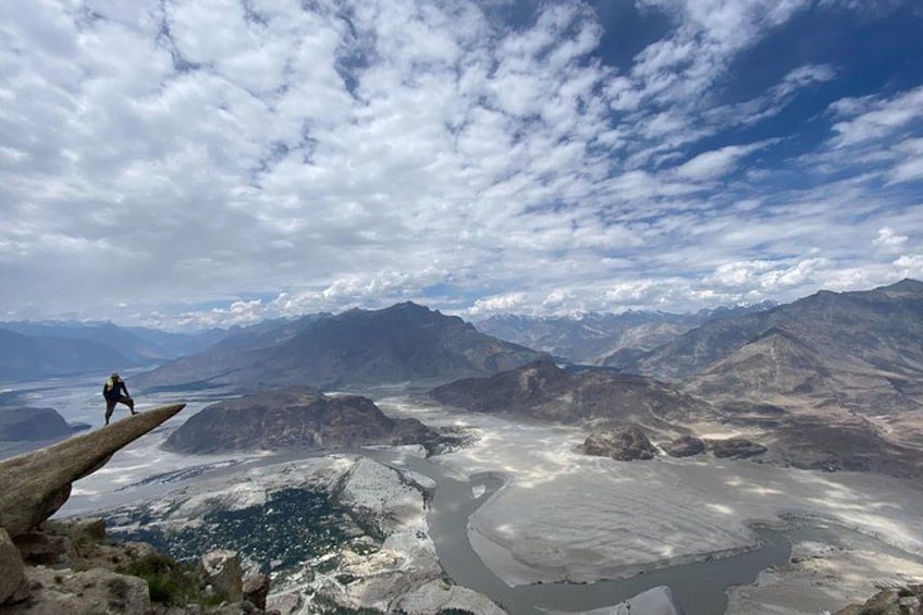 A person standing on a rock ledge overlooking a vast landscape with mountains and a river. 2