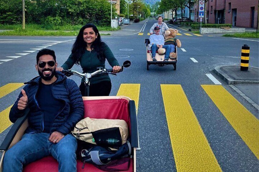 Een straat met een fietser en iemand die op een wagentje zit met een teddybeer. 2