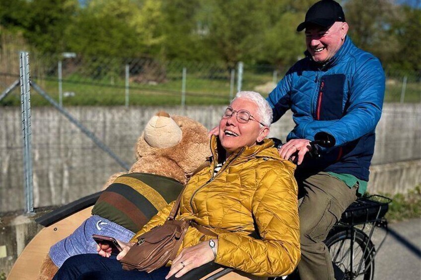 Een persoon in een geel vest zit op een fiets met een teddybeer. 3