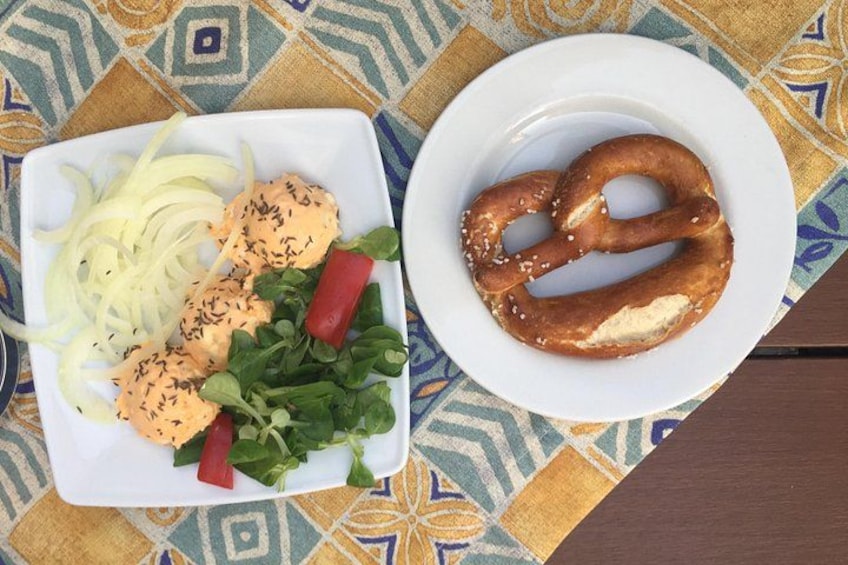 A plate with a pretzel and a salad with sliced onions and a red pepper. 1