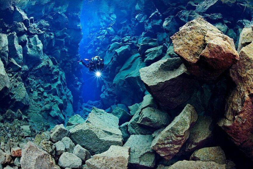 Un subacqueo esplora una grotta sottomarina rocciosa, con massi enormi e una fonte di luce. 2