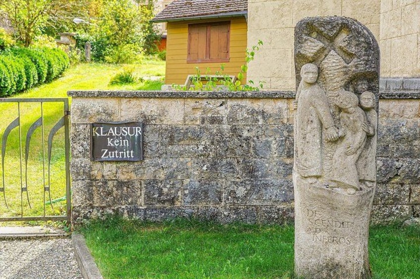 Un monumento de piedra con inscripciones, una reja de metal y un muro de piedra con una casa al fondo. 4