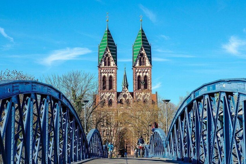 Un puente con dos torres, una iglesia de aguja verde y un cielo azul despejado. 4