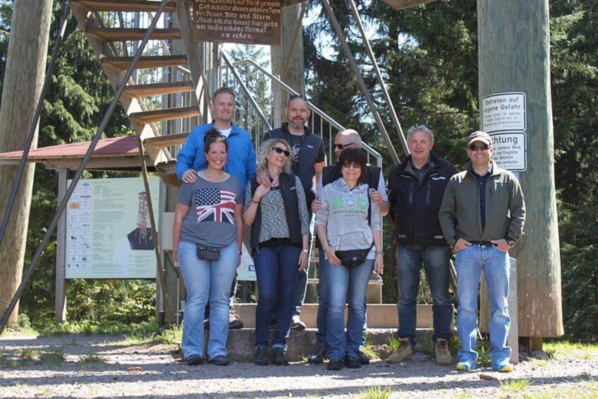 A group of people standing in front of a wooden structure with a sign. 2
