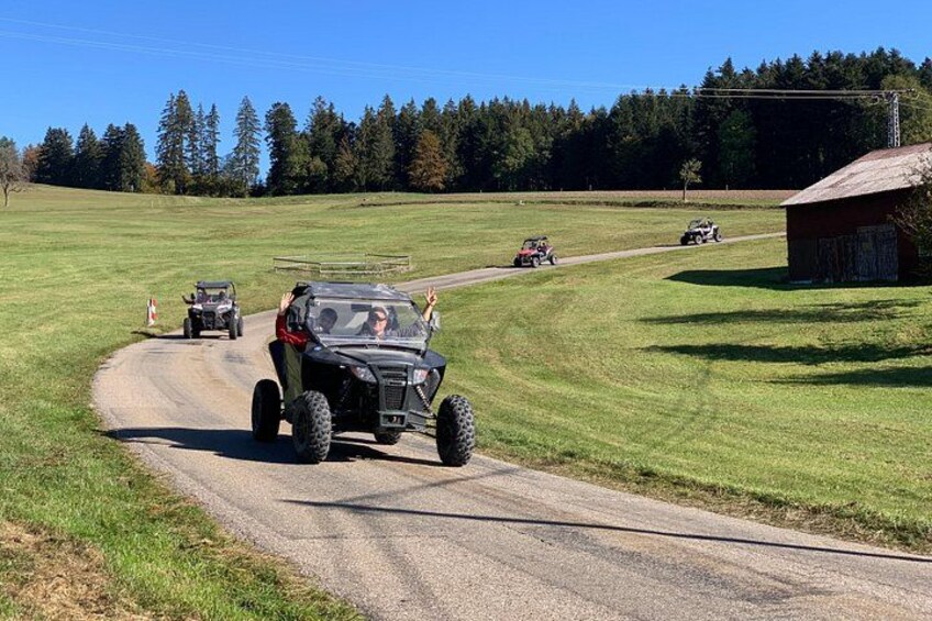 Off-road vehicles on a dirt road with a grassy field and a wooden structure in the background. 5