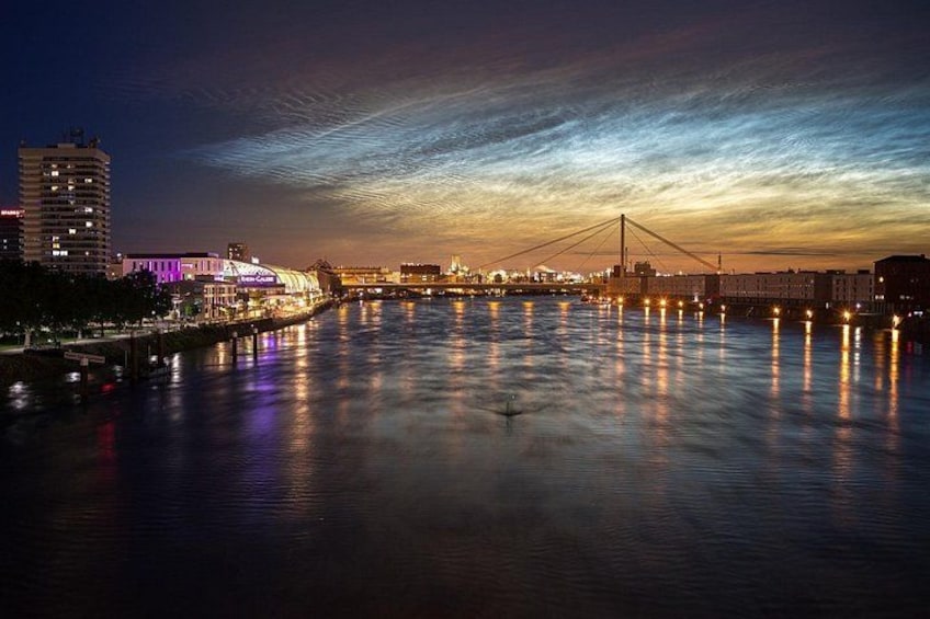 A cityscape at dusk with a lit bridge over a river, buildings along the riverbank, and a clear sky. 3