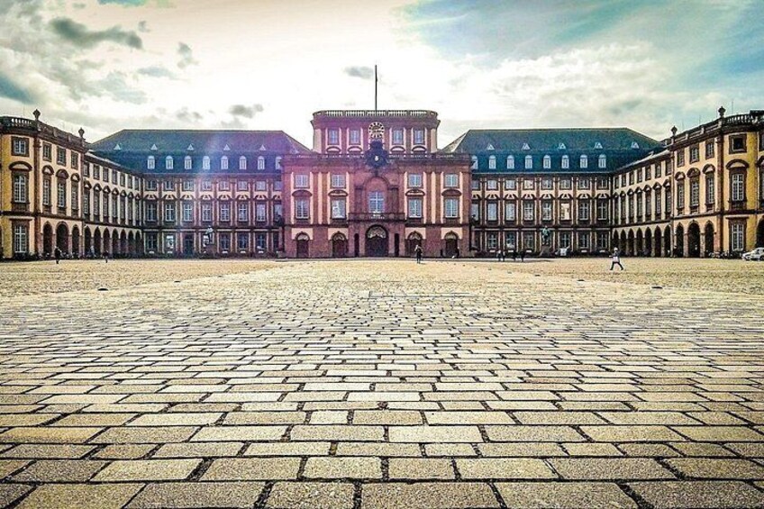 Une vaste cour ouverte, avec un bâtiment historique doté d’arcades et d’une tour centrale. 2