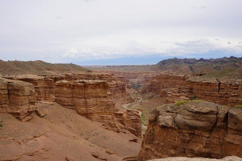 Un cañón con formaciones rocosas estratificadas y una cadena montañosa distante. 4