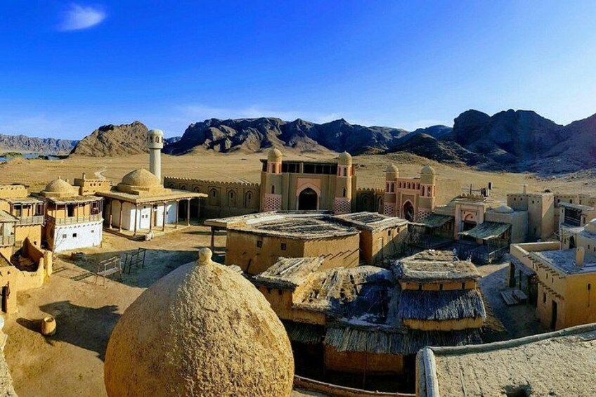 A desert village with traditional architecture, including domed buildings and a minaret. 1
