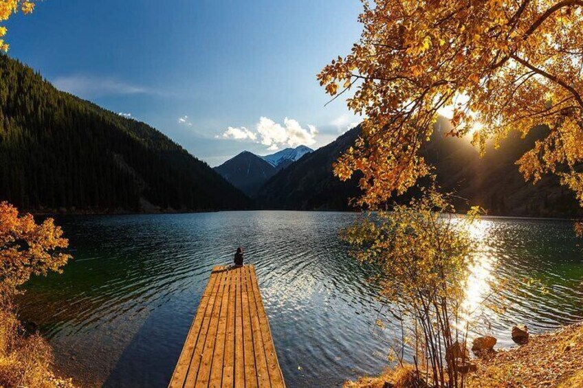 A wooden dock extending into a calm lake surrounded by autumn-colored trees and mountains. 1
