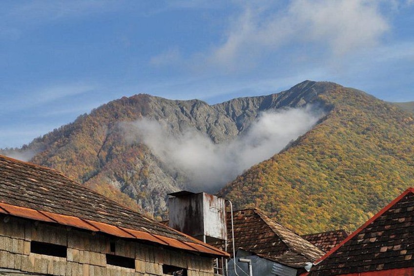 Una montaña con follaje otoñal, un edificio de madera con techo rojo y un pico cubierto de nubes. 3