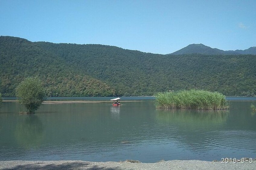 A calm lake with a small boat, surrounded by lush green hills. 2