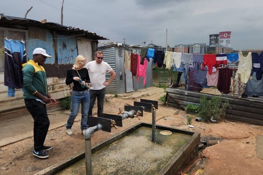 Une pompe à eau de fortune, une structure en métal ondulé et une corde à linge sur laquelle sont suspendus divers vêtements. 3