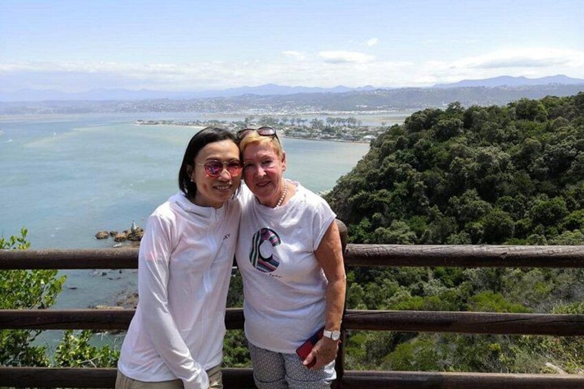 Two people standing by a railing overlooking a body of water and a distant cityscape. 2