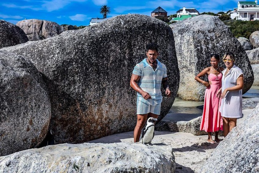 Three people standing on a rocky beach with large boulders and a surfboard. 5