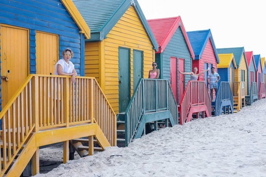 A row of colorful beach huts with wooden railings and steps leading up to them. 1