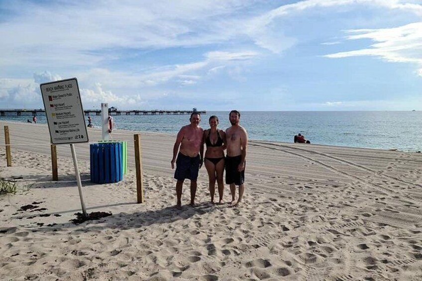 Una playa con un cartel, un muelle al fondo y cielo despejado. 5