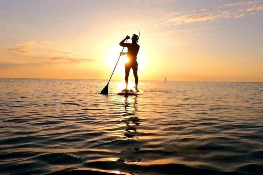 A person paddleboarding at sunset with the sun low on the horizon. 2