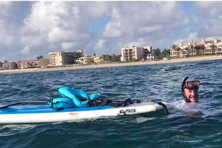 A person in a blue inflatable raft on calm water with a beach and buildings in the background. 5