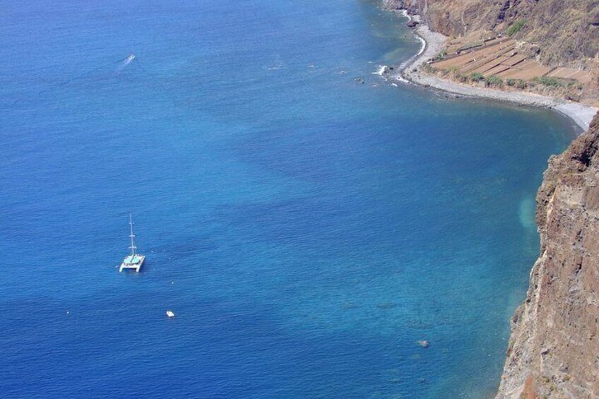 A coastal landscape with a boat anchored near the shore, clear blue waters, and a rugged cliff. 3