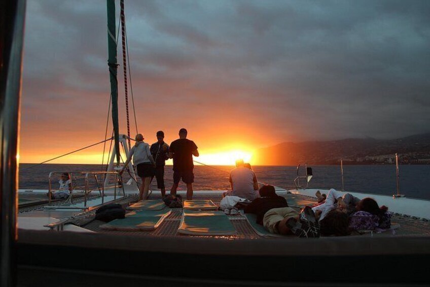 A sunset over the ocean with people relaxing on a boat deck. 1