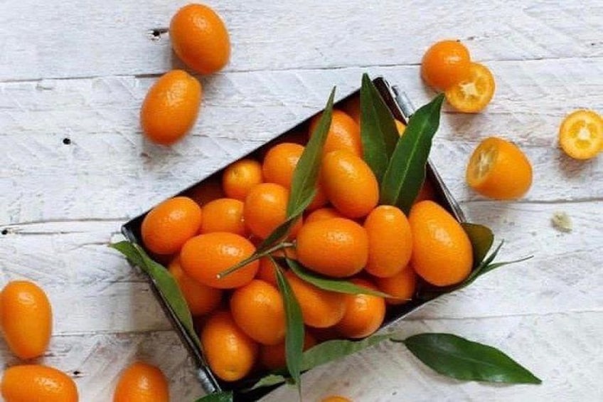 Una caja de mandarinas con hojas sobre una superficie de madera clara. 3