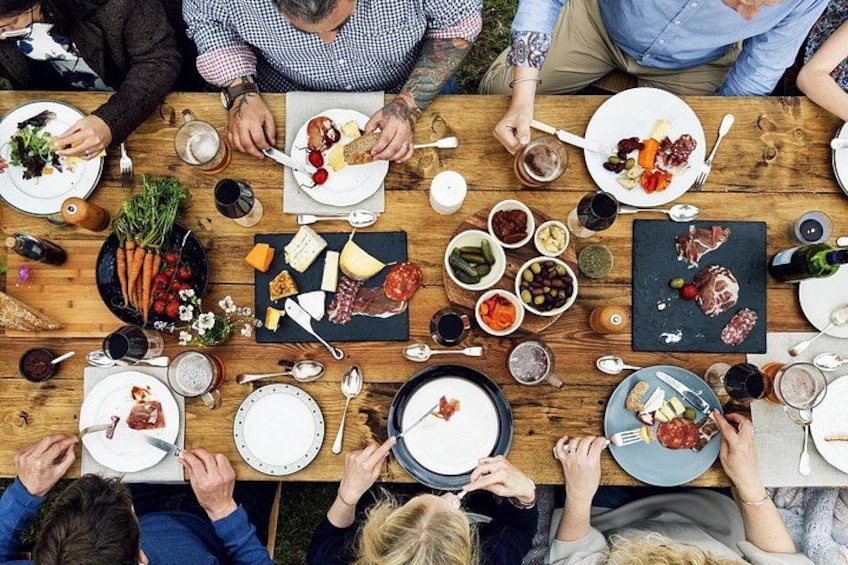 Un grupo de personas cenando en una mesa de madera con diversos alimentos y bebidas. 2