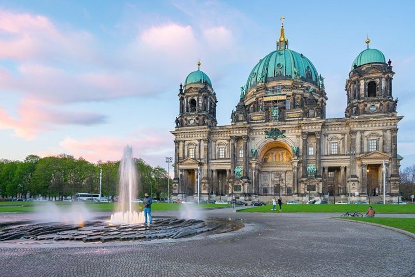 A large historic building with two domes and a fountain in front. 3