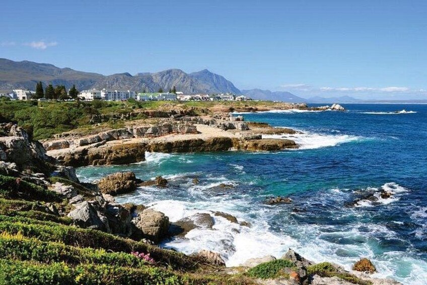 A coastal landscape with rocky terrain, clear blue sea, and distant mountains. 2