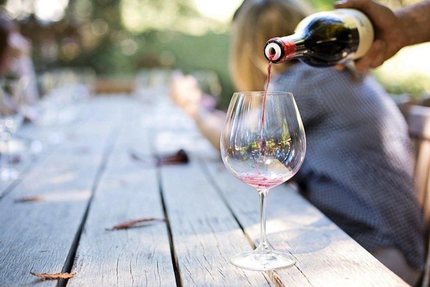 Una persona sirviendo vino tinto en una copa sobre una mesa de madera. 1