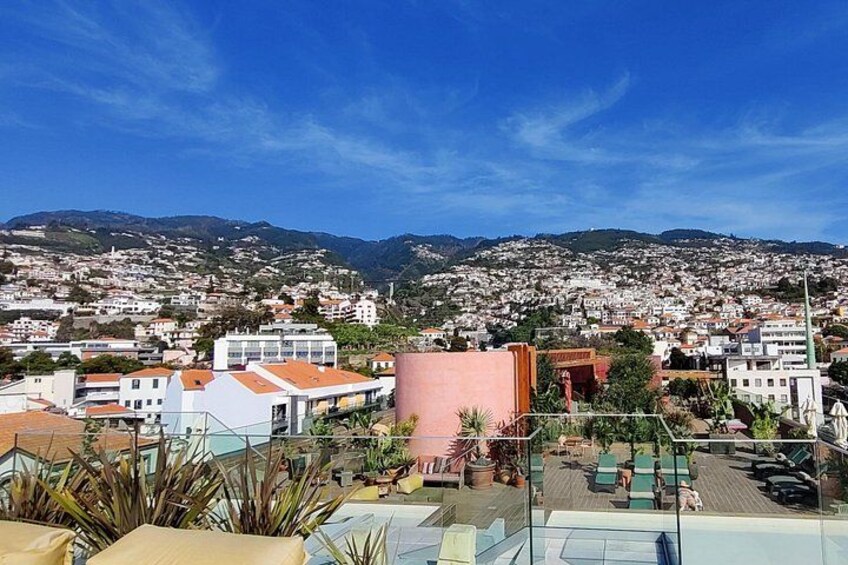 A coastal cityscape with buildings, a swimming pool, and mountains in the background. 3