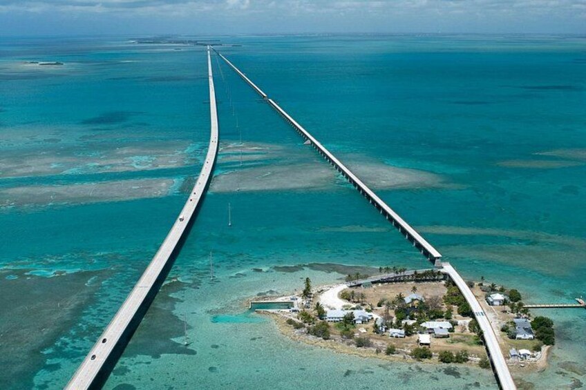 A long bridge extending over turquoise waters, with a small island with buildings and a dock in the foreground. 5