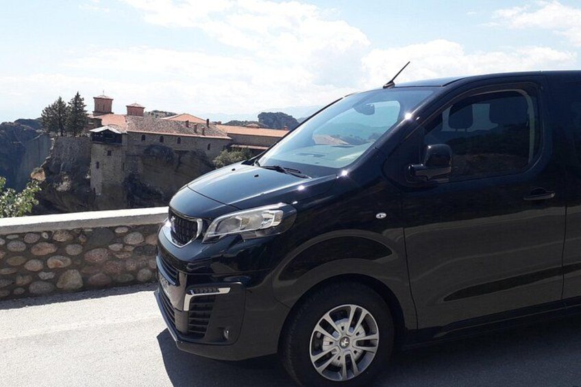 A black SUV parked on a road with a stone wall and a building in the background. 2