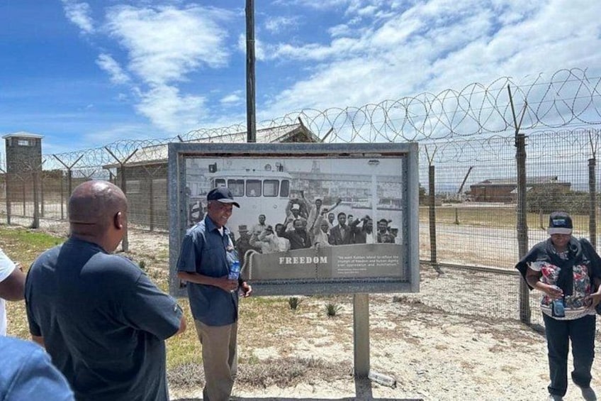 Un panneau avec une photo historique et le mot « LIBERTÉ », placé dans une zone délimitée par une clôture en fil de fer barbelé. 3