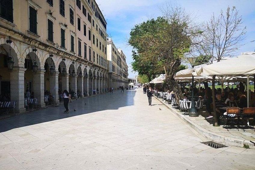 A wide pedestrian street with cafes on one side and a row of buildings with arches on the other. 2