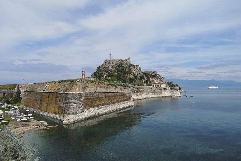 A coastal fortification with a prominent hilltop structure, a calm sea, and a clear sky. 4