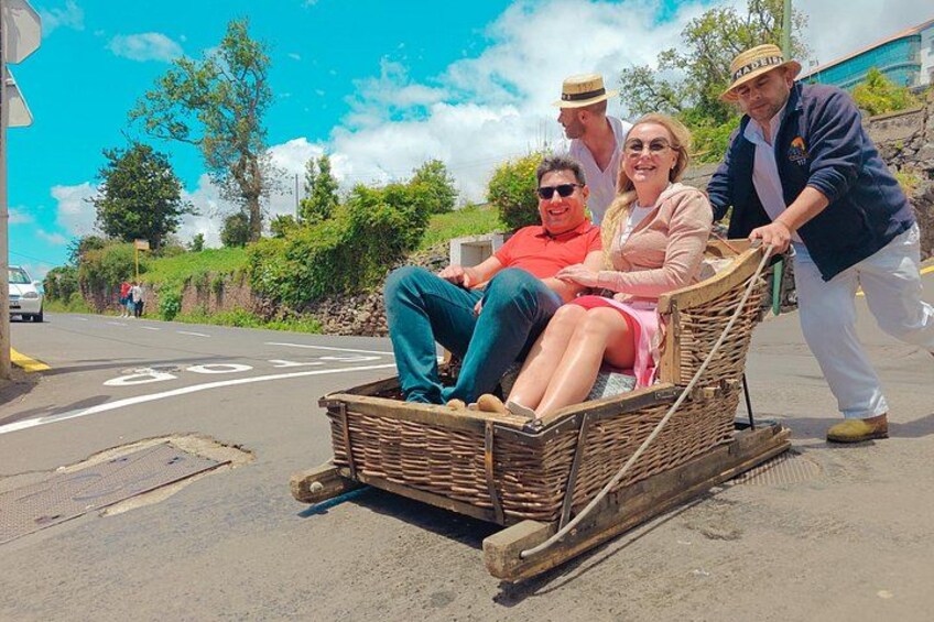 A wicker cart with two people seated and a third person pushing it. 1