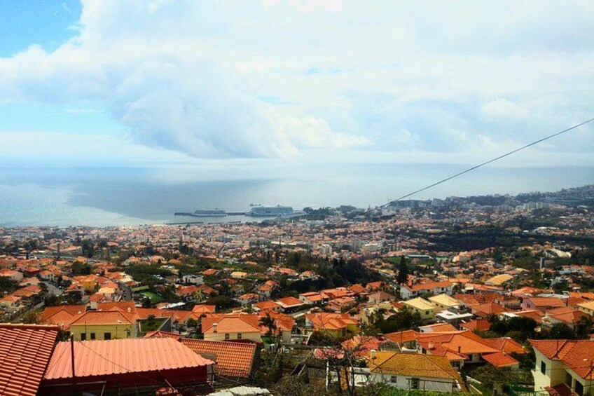 A coastal cityscape with red-roofed buildings, a large body of water, and a distant ship. 2