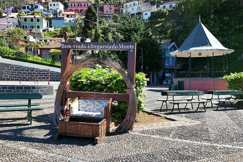 Ein Korbstuhl mit Sitzbank, ein Kiosk und ein Schild in einem Park mit Kopfsteinpflaster. 3