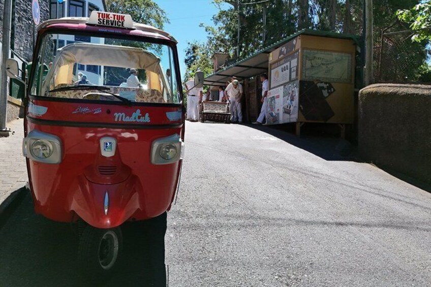 A red tuk-tuk parked on a street with a sign reading 'TUK-TUK SERVICE' and a building with a signboard in the background. 4